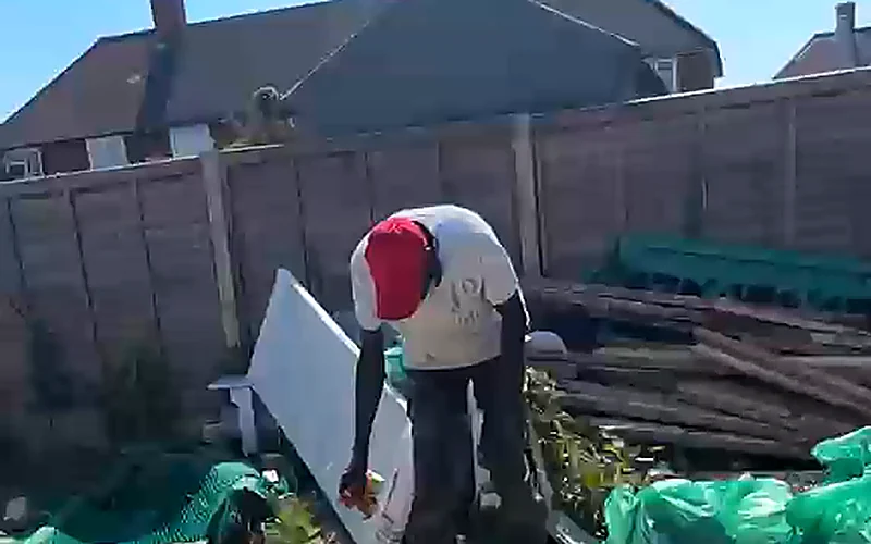 A gardener clearing timber and bagged green waste from a garden